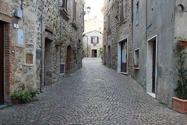 Allerona: via acciottolata nel centro storico tra case in pietra, vasi di fiori e tipici archi umbri.