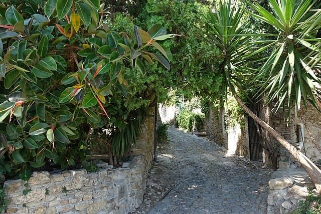 Bussana Vecchia: caruggio tra case in pietra, botteghe e archi di sostegno in fiore.
