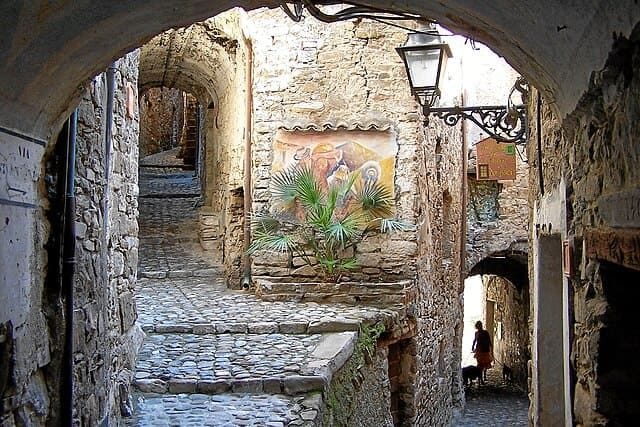 Apricale: scorcio di carruggio medievale con archi in pietra, acciottolato e fiori.