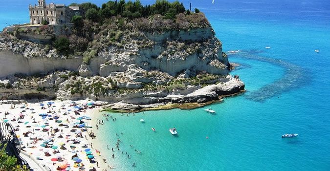 Affaccio panoramico della rupe di Tropea con i palazzi nobiliari a strapiombo sul mare turchese e il Santuario di Santa Maria dell’Isola.