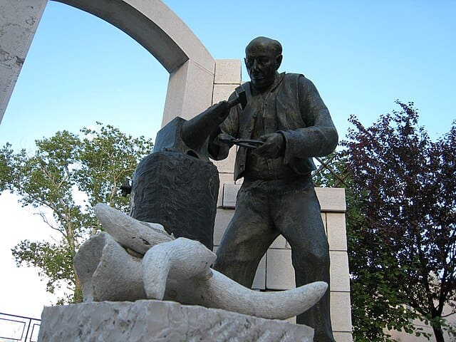 Questa scultura in bronzo raffigura un fabbro al lavoro mentre batte un martello su un'incudine.