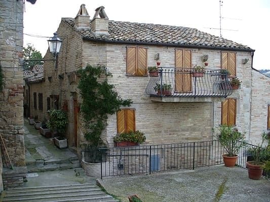 Facciata esterna di una casa tipica in mattoni rossi a Torre di Palme, con fiori alle finestre e architettura medievale marchigiana.