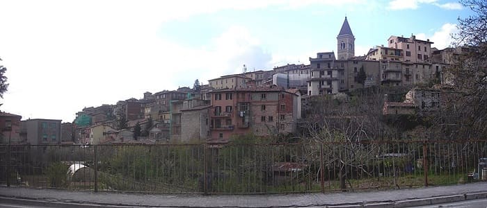 Veduta panoramica del borgo medievale di Gualdo Tadino in Umbria con le tipiche case in pietra disposte sui colli e le montagne appenniniche sullo sfondo.