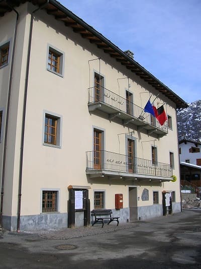 Facciata esterna del Municipio di Saint-Rhémy-en-Bosses in Valle d'Aosta con montagne innevate sullo sfondo.