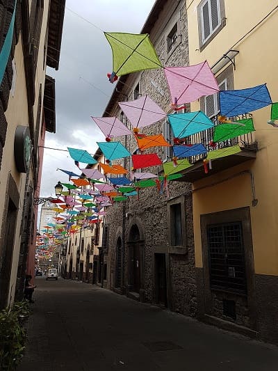 Via del centro storico di Vitorchiano addobbata a festa con bandiere e decorazioni tradizionali tra le case in pietra di peperino