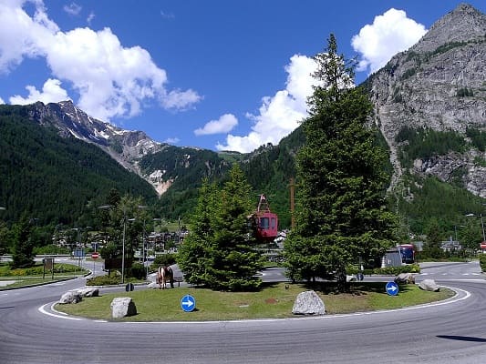 Rotonda di benvenuto all'ingresso di Courmayeur con lo sfondo delle montagne alpine e del Monte Bianco.