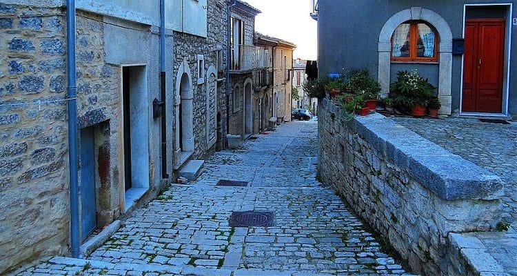 Scorcio di un vicolo in pietra nel centro storico di Oratino in Molise, con archi medievali, piante fiorite e case antiche.