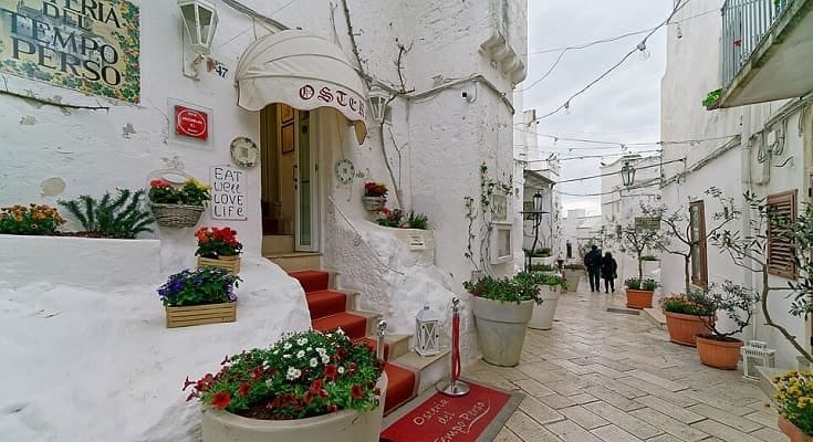 Vicolo fiorito nel centro storico di Ostuni con case bianche in calce e vasi di gerani rossi